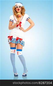 Creative retro photo of a fashionable pin-up sailor girl, wearing a cool garrison cap, holding an ice cream in a waffle cone and posing on blue background.