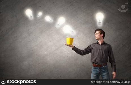 Creative sandbox. Young man in casual and light bulbs from bucket