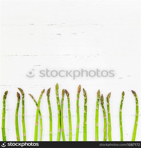 Creative scandinavian style flat lay top view mockup of fresh green asparagus on white wooden table frame background copy space. Minimal house cooking concept mock up for blog or recipe book