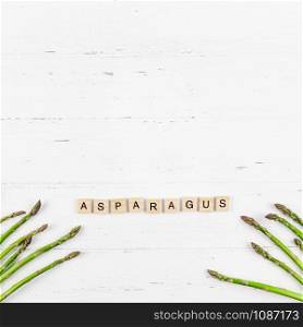 Creative scandinavian style flat lay top view mockup of fresh green asparagus on white wooden table frame background copy space. Minimal house cooking concept mock up for blog or recipe book