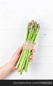 Creative scandinavian style flat lay top view of fresh green asparagus in woman hands on white wooden table background copy space. Minimal house cooking concept for blog or recipe book
