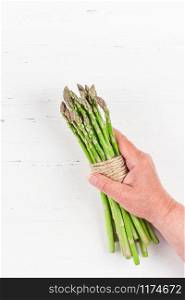 Creative scandinavian style flat lay top view of fresh green asparagus in elderly woman hands on white wooden table background copy space. Minimal house cooking concept for blog or recipe book
