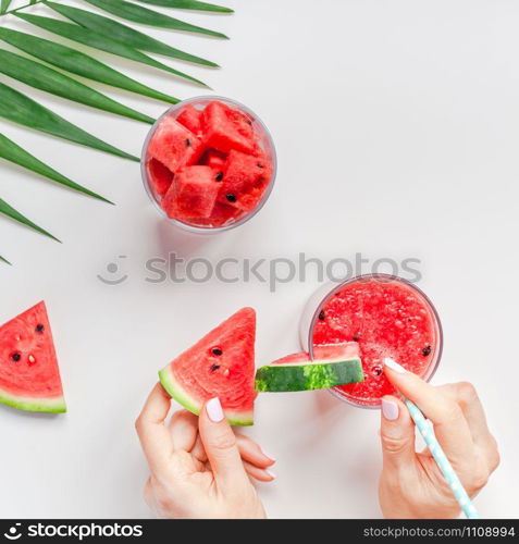 Creative scandinavian style flat lay top view of fresh watermelon slices smoothie drink in glass woman hands on white table background copy space. Minimal summer fruits concept for blog or recipe book