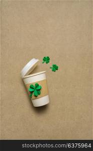 Creative St. Patricks Day concept photo of take away coffee cup with shamrocks made of paper on brown background.