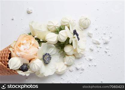 Creative still life of an ice cream waffle cone with flowers and meringues on white background.. Waffle cone with composition of flowers