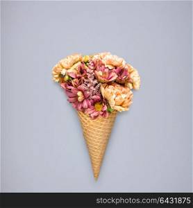 Creative still life of an ice cream waffle cone with flowers on grey background.