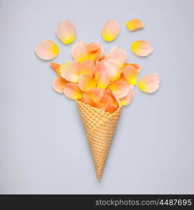 Creative still life of an ice cream waffle cone with rose petals on grey background.