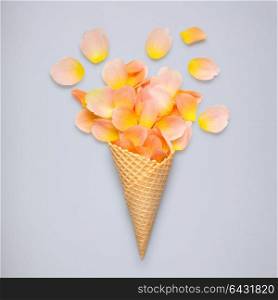 Creative still life of an ice cream waffle cone with rose petals on grey background.