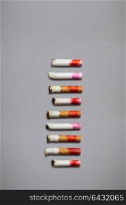 Creative still life of different cigarette stubs with lipstick on grey background.