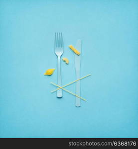 Creative still life photo of fork and spoon with raw pasta on blue background.