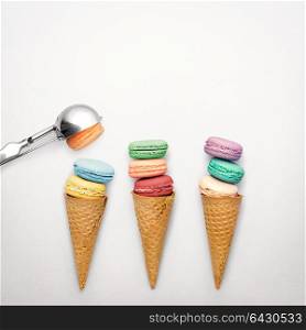 Creative still life photo of three waffle cones with macaroons and spoon on grey background.