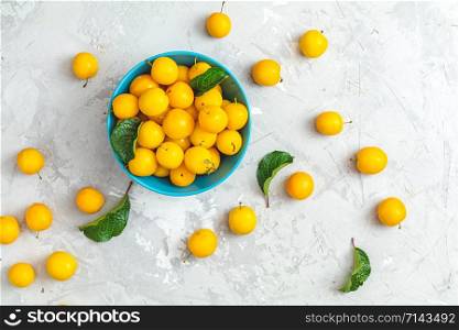Creative summer pattern made of fresh yellow cherry plums in blue bowl on gray concrete background. Fruit minimal concept. Flat lay.