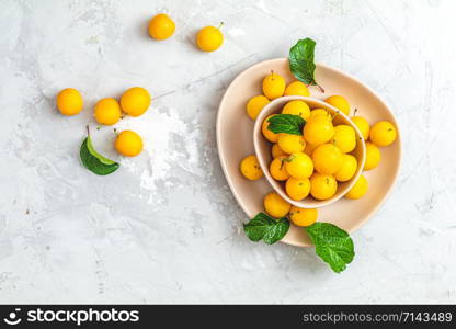 Creative summer pattern made of fresh yellow cherry plums in pink bowl on gray concrete background. Fruit minimal concept. Flat lay.