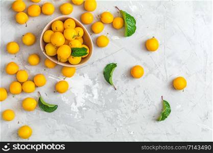 Creative summer pattern made of fresh yellow cherry plums in pink bowl on gray concrete background. Fruit minimal concept. Flat lay.