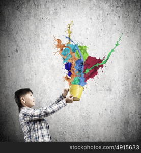 Creative thinking. Young boy splashing colorful paint from bucket