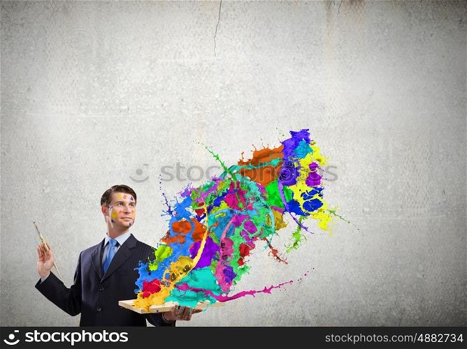 Creative thinking. Young businessman with brush in hand and colorful paint splashes