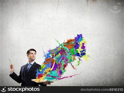Creative thinking. Young businessman with brush in hand and colorful paint splashes
