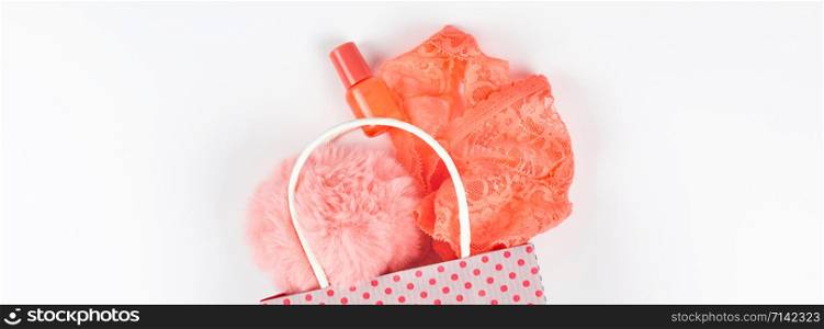 Creative top view flat lay of coral color accessories and lingerie in shopping bag with copy space on white background in minimal style. Concept feminine blog social media