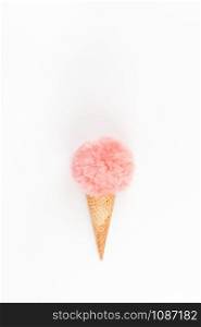 Creative top view flat lay of coral color fluffy fur ball in ice cream waffle cone with copy space on white background in minimal style. Concept feminine blog social media. Natural light with shadows