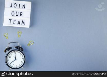 Creative top view flat lay of desk with Join our team text on lightbox with copy space on blue background in minimal style. Concept of new job, hiring recruitment process, new team members screening