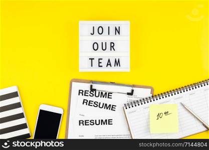 Creative top view flat lay of desk with join our team text on lightbox copy space on bold yellow background in minimal style. Concept of new job, hiring recruitment process, new team members screening