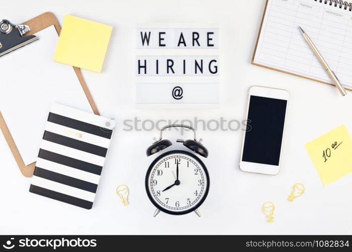 Creative top view flat lay of desk with we are hiring text on lightbox with copy space on white background in minimal style. Concept of new job, hiring recruitment process, new team members screening