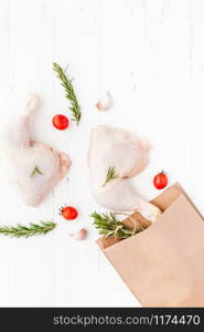 Creative Top view flat lay of fresh raw chicken legs with rosemary herbs garlic tomatoes on white wooden background with copy space. Food preparation recipe cooking concept
