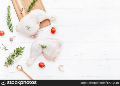Creative Top view flat lay of fresh raw chicken legs with rosemary herbs garlic tomatoes on white wooden background with copy space. Food preparation recipe cooking concept