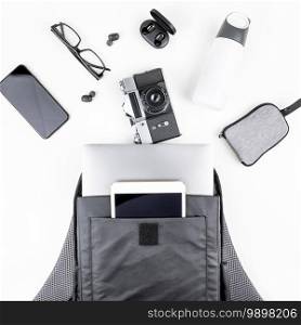 Creative top view flat lay of open backpack with laptop and tablet inside, mobile phone, copy space white background minimal style. Concept of modern man accessories for education, business and life