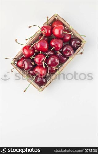 Creative top view of fresh ripe cherry in a small wicker basket with copy space isolated white background minimal style. Concept of summer fun and healthy eating. Template for your text or food design