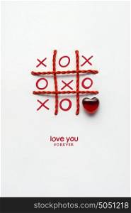 Creative valentines concept photo of noughts and crosses game with heart on white background.