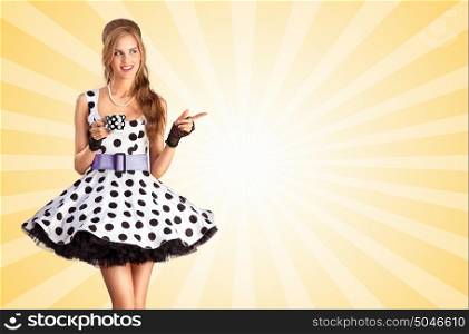 Creative vintage photo of a beautiful pin-up girl in a polka dot dress, holding a cup of tea and pointing aside on colorful abstract cartoon style background.