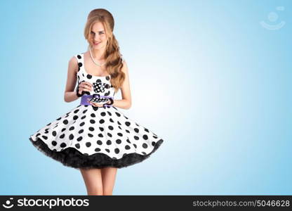 Creative vintage photo of a beautiful pin-up girl in a polka dot dress, holding a cup of tea and smiling on blue background.