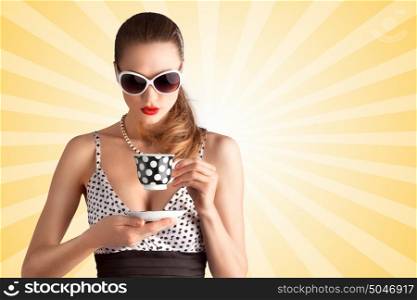 Creative vintage photo of a beautiful pin-up girl in a polka dot bikini and sunglasses, drinking tea or coffee on colorful abstract cartoon style background.