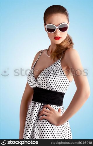 Creative vintage portrait of a beautiful pin-up girl wearing a fashionable retro dress in polka dots on blue background.