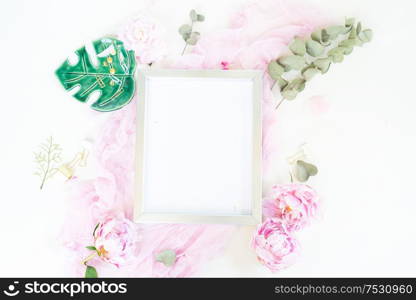 Creative wedding composition with metalic photo frame mock up, pink blanket, flowers on white desk background. Flat lay, top view stylish art concept.. Creative wedding composition