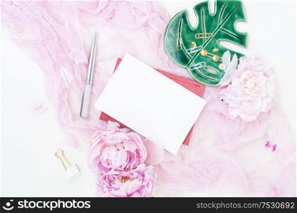 Creative wedding composition with wedding invitation mock up, pink blanket, flowers, eucalyptus branches and brushes on white background. Flat lay stylish art concept with copy space on white card.. Creative wedding composition
