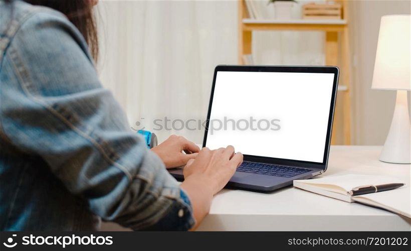 Creative young asia woman sitting at Her desk using laptop with mock up white screen in the cozy living room at modern home.
