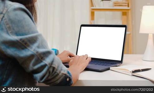 Creative young asia woman sitting at Her desk using laptop with mock up white screen in the cozy living room at modern home.