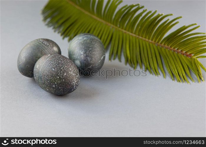 Creatively painted chicken Easter eggs with natural hibiscus dye, look like sea stones, date palm leaf on gray background, copy space. Happy creative Easter concept. Soft slective focus. Side view.