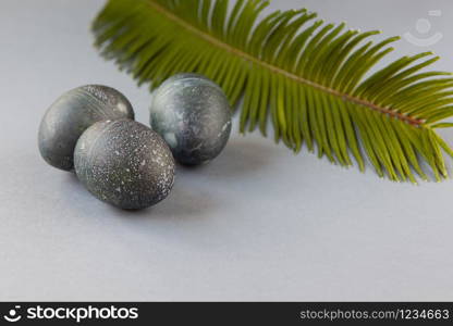 Creatively painted chicken Easter eggs with natural hibiscus dye, look like sea stones, date palm leaf on gray background, copy space. Happy creative Easter concept. Soft slective focus. Side view.