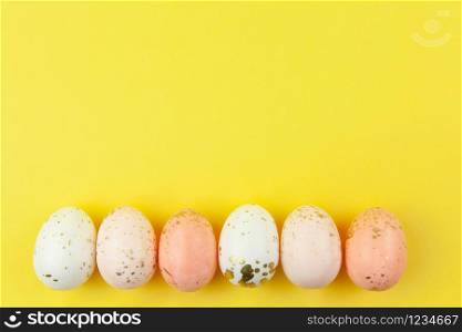 Creatively painted eggs in pastel colors decorated with gold leaf are arranged in row along bottom edge on yellow background, copy space. Happy Easter DIY concept. Flat lay. Horizontal.