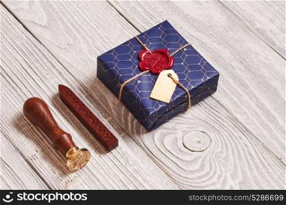 Creatively wrapped and decorated christmas present in box and wax seal stamp on white wooden background