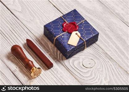 Creatively wrapped and decorated christmas present in box and wax seal stamp on white wooden background