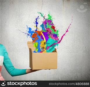 Creativity concept. Close up of female hand holding carton box with colorful splashes
