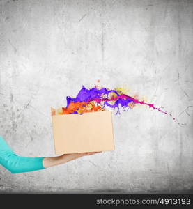 Creativity concept. Close up of female hand holding carton box with colorful splashes