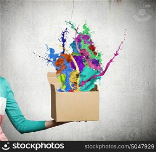 Creativity concept. Close up of female hand holding carton box with colorful splashes