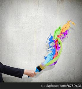 Creativity concept. Close up of hand holding brush with colorful paint splashes