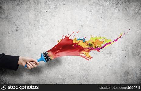 Creativity concept. Close up of hand holding brush with colorful paint splashes