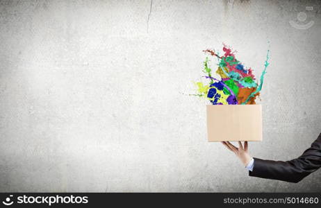 Creativity concept. Close up of hand holding carton box with colorful splashes